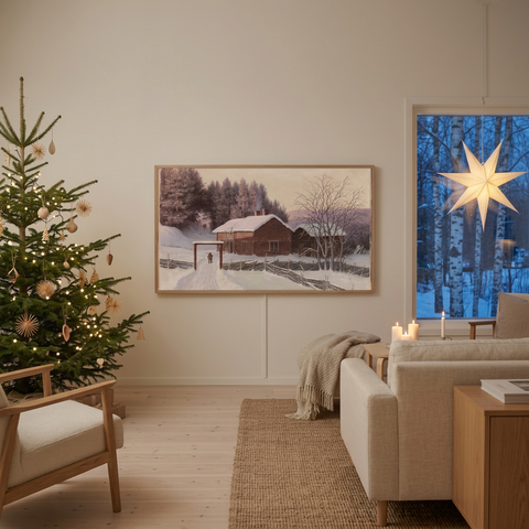 A framed winter landscape print hangs on a beige wall in a modern, cozy living room. The print depicts a snowy scene with a rustic cabin, bare trees, and a soft purple sky.